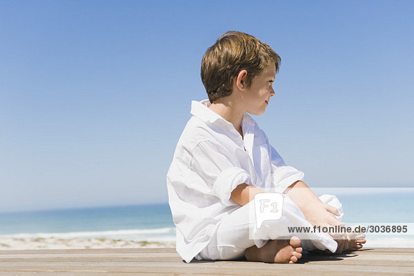 Boy sitting on a boardwalk on the beach