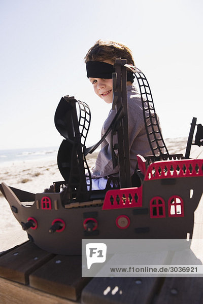Junge in Piratenkostüm spielt mit einem Spielzeugboot