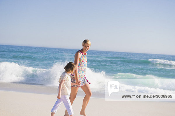 Frau  die mit ihrer Tochter am Strand spazieren geht.