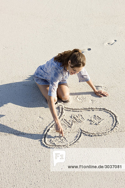 Frau beim Zeichnen einer Herzform am Strand