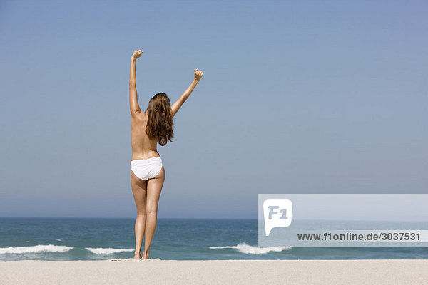 Rückansicht einer am Strand stehenden Frau mit erhobenen Armen