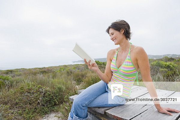 Frau sitzt auf einer Promenade und liest ein Buch.