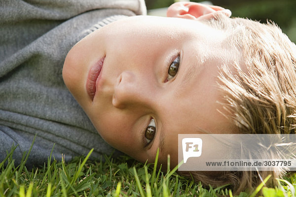 Junge liegt auf Gras und sieht ernst aus.