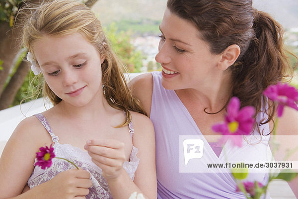 Nahaufnahme einer Frau  die mit ihrer Tochter lächelt und eine Blume hält.