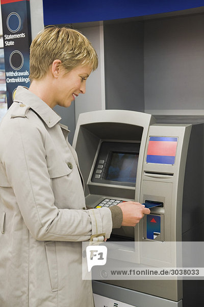 Frau  die eine Kreditkarte in Geldautomat einführt