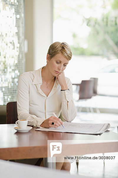 Geschäftsfrau sitzt in einem Restaurant und liest eine Finanzzeitung.