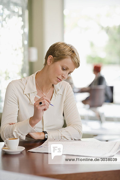 Businesswoman sitting in a restaurant and reading a financial newspaper