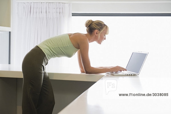 Woman leaning on a counter and working on a laptop