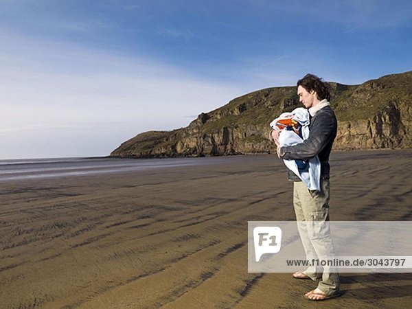 Mann am Strand hält Baby