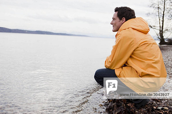 Mann im Regenmantel am Ufer sitzend