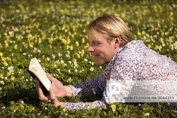 Mann liest im Gras mit Frühlingsblumen