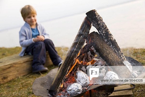 Junge schaut Kartoffeln an Grillfeuer