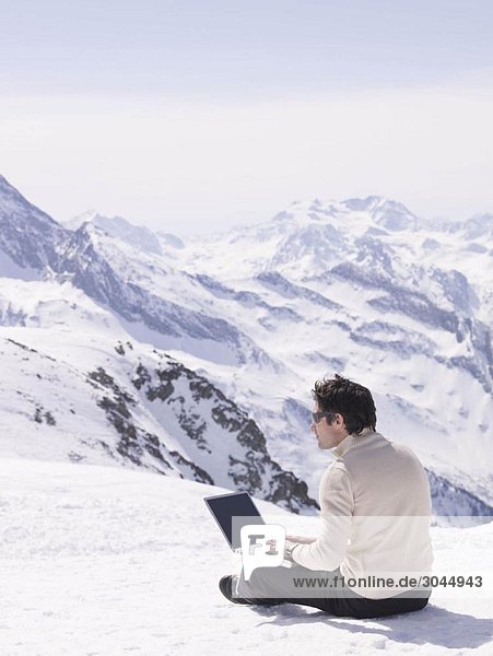 man sitting in the snow using laptop