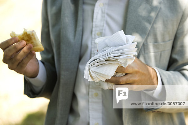 Person holding half eaten pastry in one hand and disposable cup and paper napkins in other hand