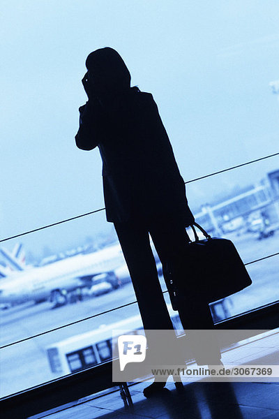 Silhouette der Frau Reisende mit dem Handy  hält Reisetasche im Flughafen
