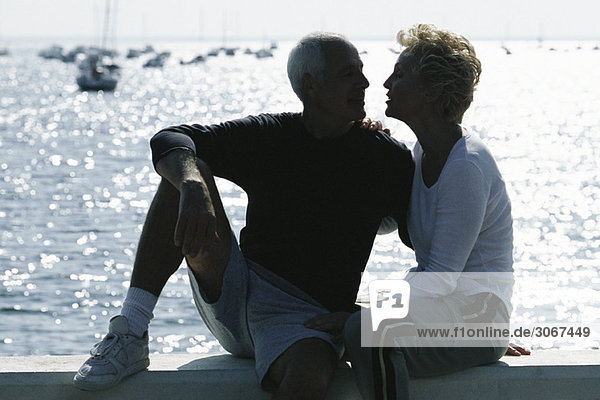 Mature couple sitting together on pier  backlit