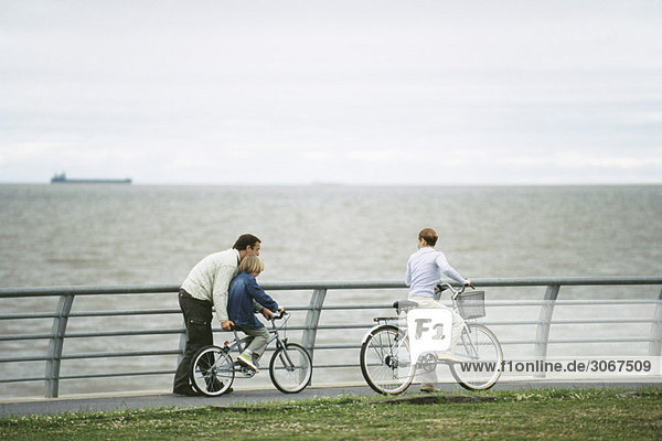 Vater hilft Sohn Fahrrad fahren lernen  Mutter beobachtet