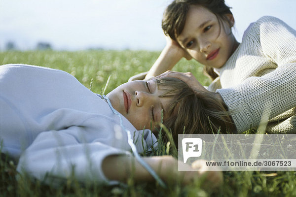 Schwester und Bruder liegen zusammen im Gras  das Mädchen berührt den Kopf des schlafenden Jungen.