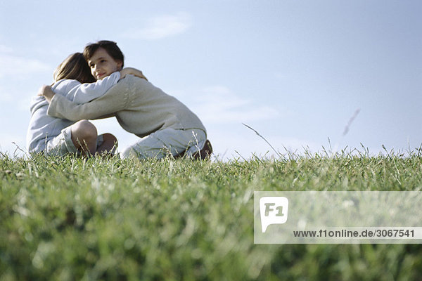 Mädchen umarmt ihren jüngeren Bruder im Grasfeld