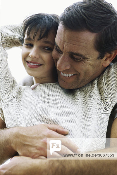 Vater umarmt Tochter von hinten  Wange zu Wange  beide lächelnd