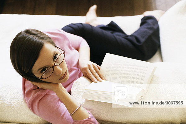 Woman sitting on sofa reading book  looking up at camera  high angle view