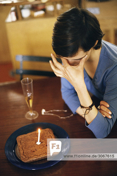 Woman sitting at table alone with anniversary cake  covering eyes