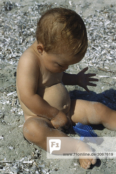 Kleinkind sitzt nackt am Strand und entdeckt sich selbst.