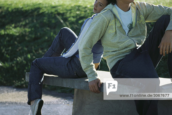 Junges Paar sitzt Rücken an Rücken auf Parkbank