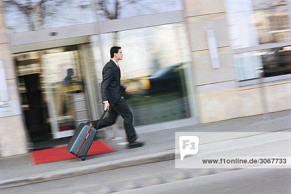 Ein Geschäftsmann rennt den Bürgersteig hinunter und zieht den Koffer hinter sich her.