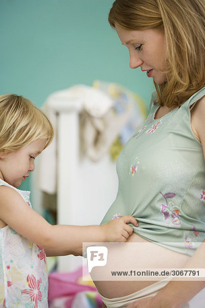Kleines Mädchen schaut auf Mutters schwangeren Bauch