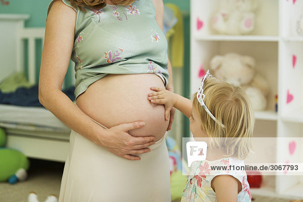 Kleines Mädchen berührt Mutters schwangeren Bauch