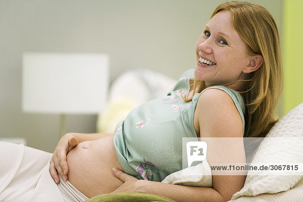 Schwangere Frau entspannt auf dem Bett  lächelnd