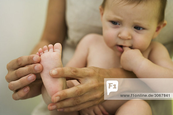 Mother holding baby on lap  playing with baby's foot  cropped