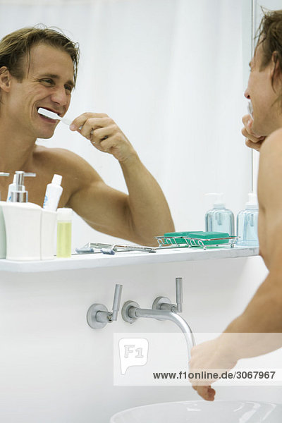 Mann putzt Zähne  schaut sich selbst im Spiegel an