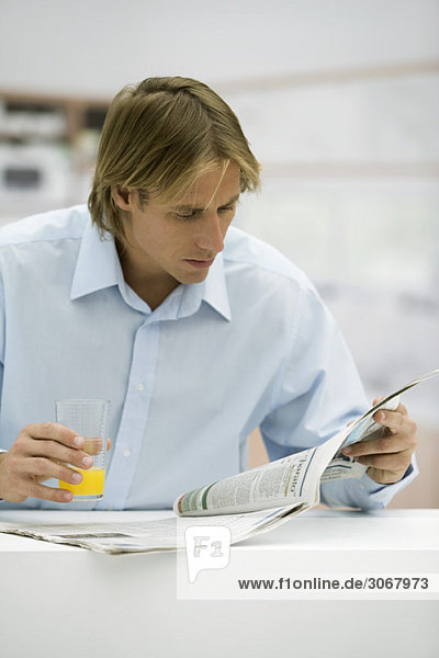 Mann mit einem Glas Saft beim Blick auf die Zeitung