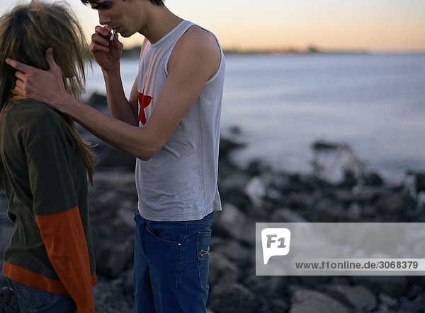 Junges Paar stehend von Angesicht zu Angesicht  rauchend  am Wasserrand  Seitenansicht