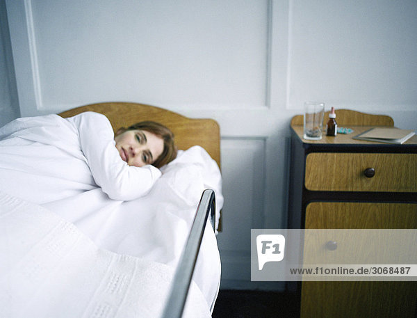 Woman lying in hospital bed  hand under her head  looking at camera