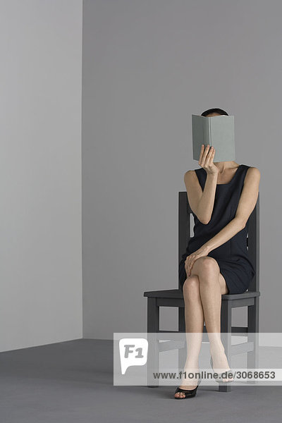 Frau im Sessel sitzend  offenes Buch vor dem Gesicht haltend