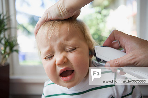Erwachsener legt Thermometer ins Ohr des weinenden Babys