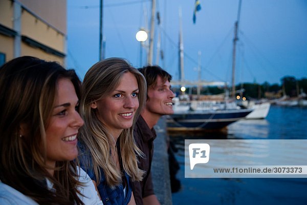 Three friends sitting on a quay-edge Stockholm Sweden.