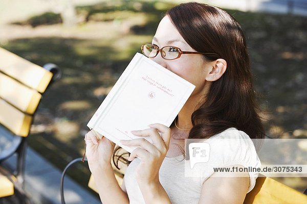 Junge Frau ihr Gesicht mit Buch ausblenden