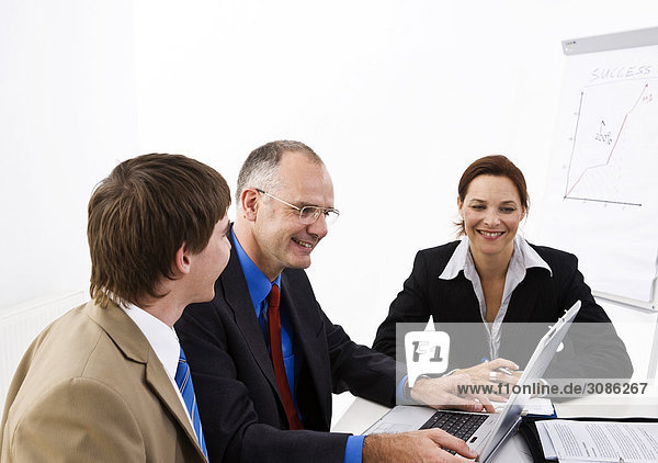 Geschäftsleute an einem Tisch sitzend  schauen auf einen Laptop
