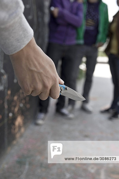 Junger Mann mit einem Taschenmesser  Teenager im Hintergrund