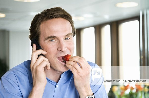 Mann spricht im Telefon und isst Erdbeere