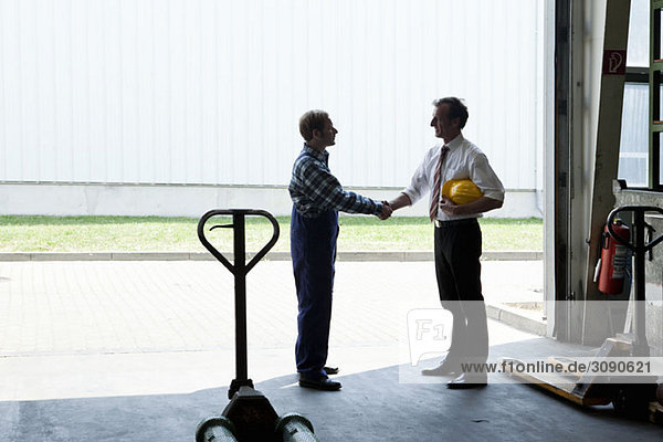 A manual worker shaking hands with a manager in a metal parts warehouse