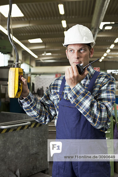 A factory worker using a walkie-talkie and operating a factory machine