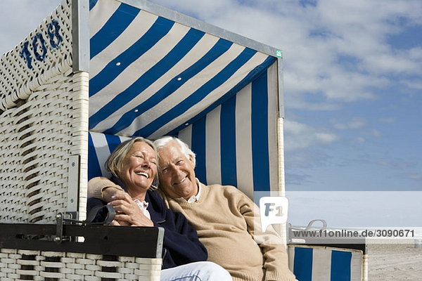 Ein älteres Paar sitzt zusammen in einem Strandkorb mit Kapuze.