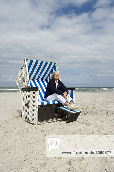Eine ältere Frau  die in einem Strandstuhl mit Kapuze sitzt.