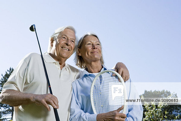 Ein älteres Paar mit einem Golfschläger und einem Tennisschläger.
