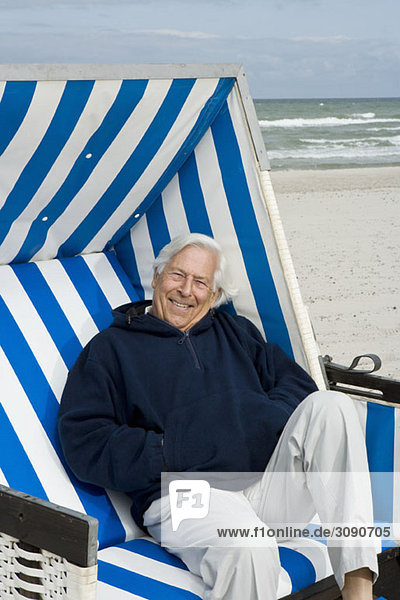 Ein älterer Mann sitzt auf einem Strandstuhl mit Kapuze.